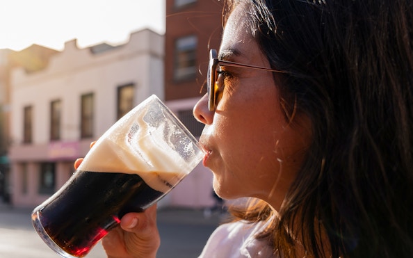 Woman enjoying a pint of dark beer outdoors in a city setting.