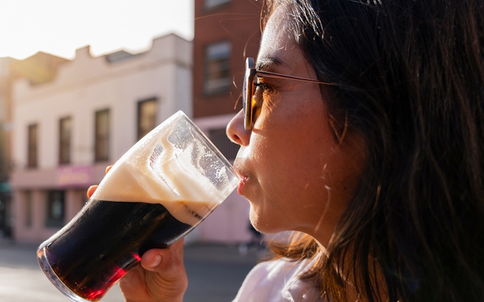 Woman enjoying a pint of dark beer outdoors in a city setting.