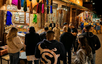 Tour group exploring vibrant Marrakech souk with colorful textiles and spices.