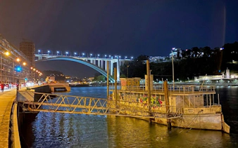 Night view of Porto's illuminated bridge over the Douro River with graffiti-covered dock.