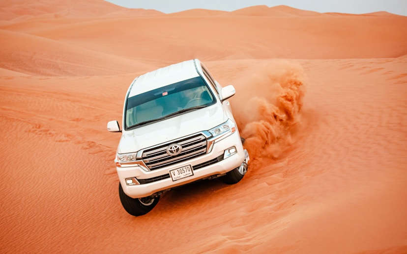 SUV driving through sand dunes in Doha desert, Qatar.