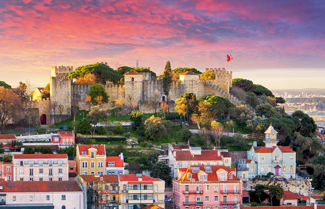 São Jorge Castle in Lisbon at sunset with cityscape in the background.