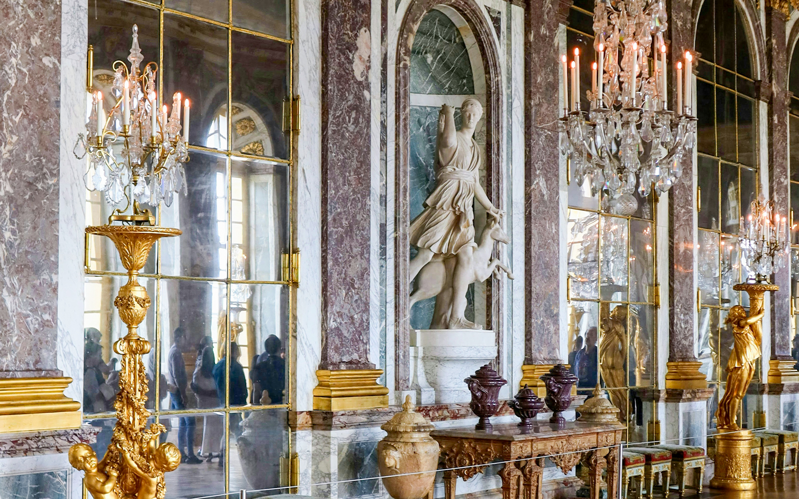 Palace of Versailles interior with ornate chandeliers and classical statue.