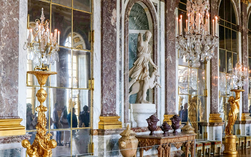 Palace of Versailles interior with ornate chandeliers and classical statue.