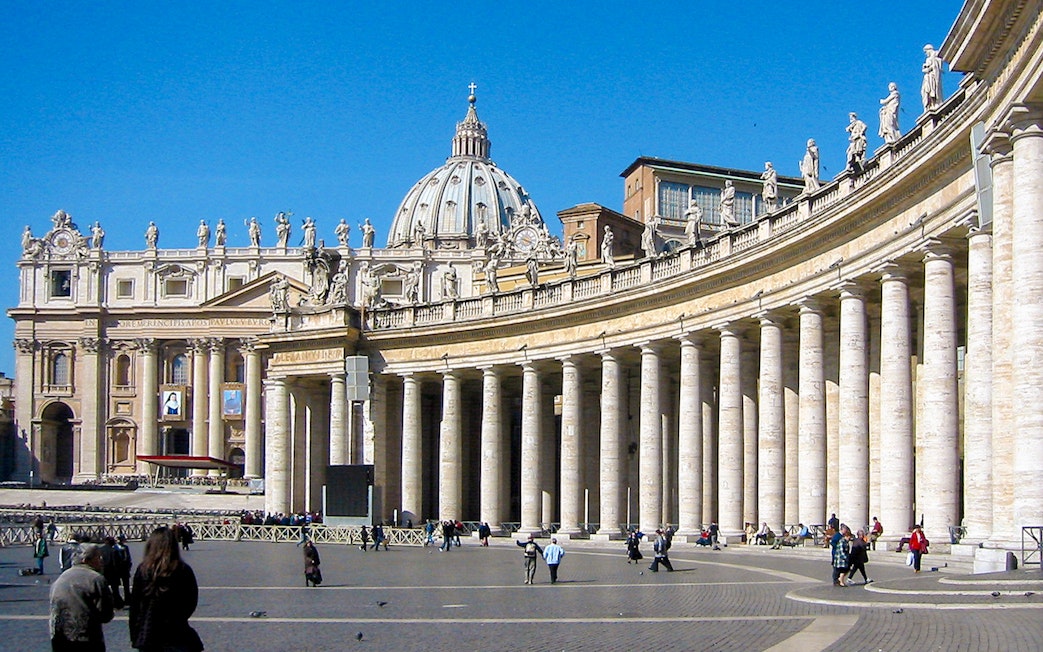 Tourists walking in St. Peter's Square with St. Peter's Basilica in Vatican City.
