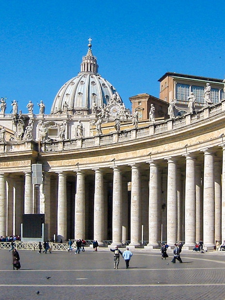 Tourists walking in St. Peter's Square with St. Peter's Basilica in Vatican City.