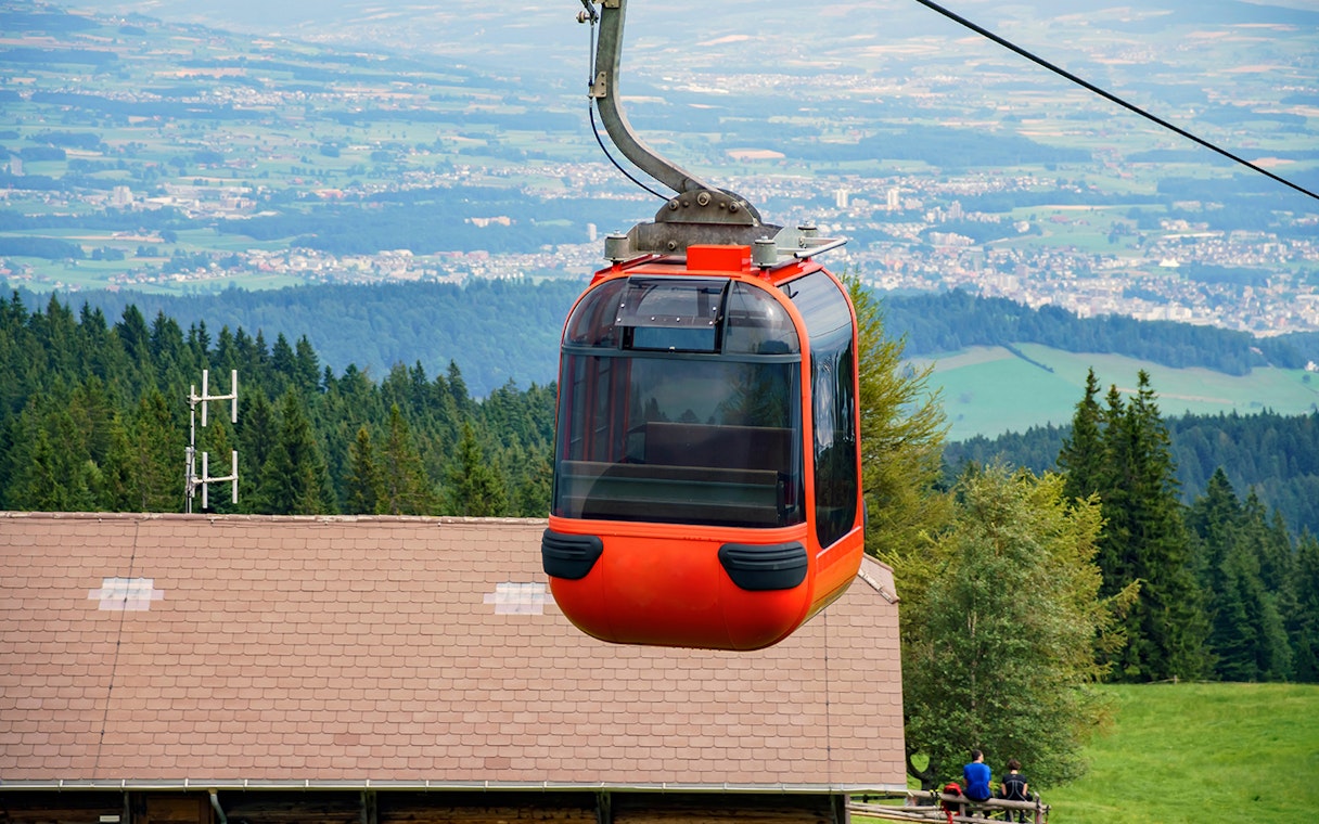 Mount Pilatus cable car ascending over lush green landscape and distant city view.