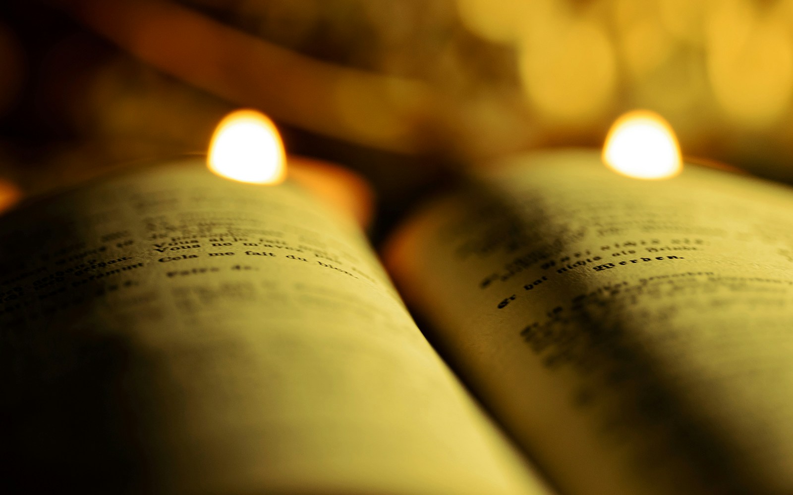 Open old book with text illuminated by candlelight.
