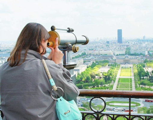 Woman viewing Paris through a telescope from the Eiffel Tower