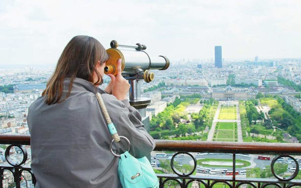 Woman using telescope to view Paris from Eiffel Tower.