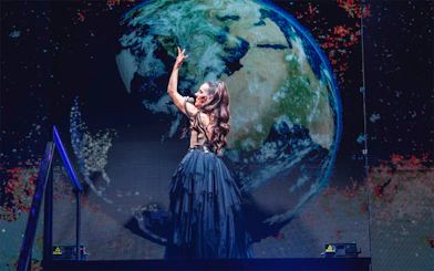 Performer on stage with Earth backdrop, WAH tour.