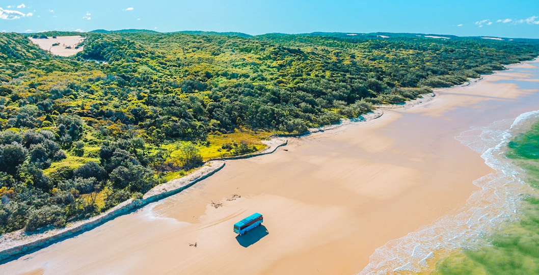 4 wheel drive coach on K'gari's Fraser Island beach, showcasing coastal tour experience.