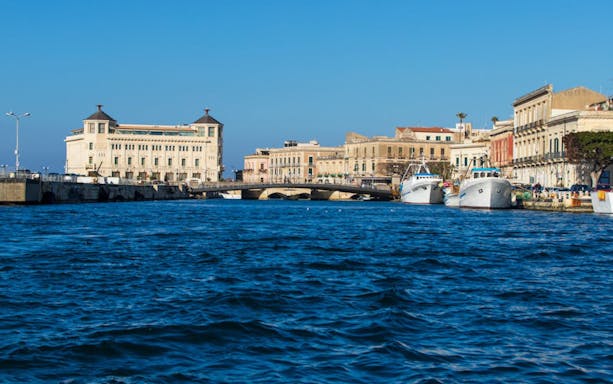 Ortigia waterfront with historic buildings and boats docked along the shore.