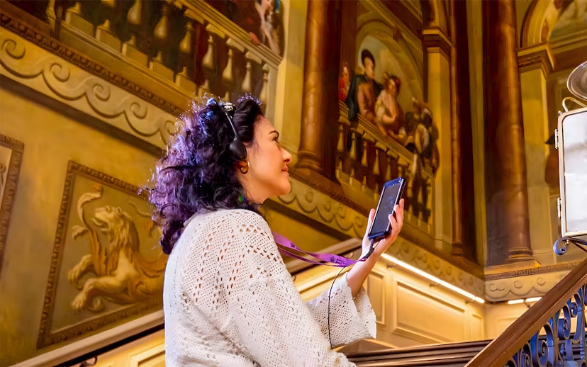 Visitor using audio guide at Kensington Palace staircase.