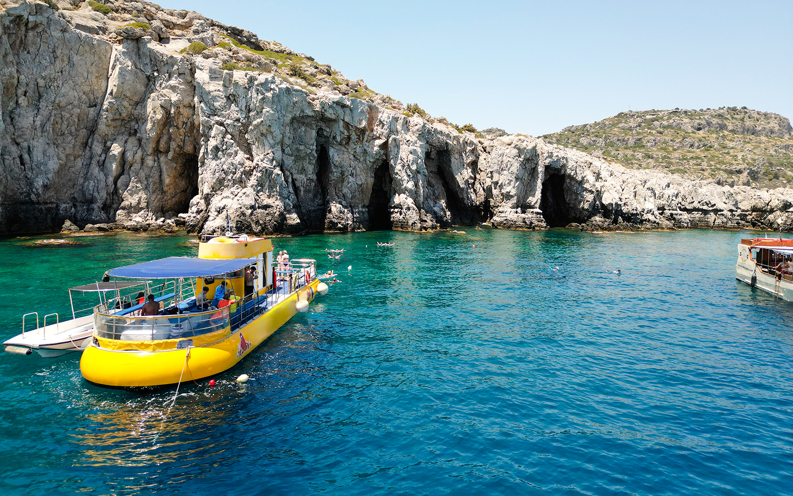 Yellow submarine cruise near rocky coast of Rhodes, Greece, with swimmers in clear blue water.