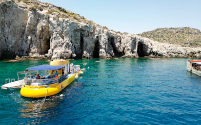 Yellow submarine cruise near rocky coast of Rhodes, Greece, with swimmers in clear blue water.
