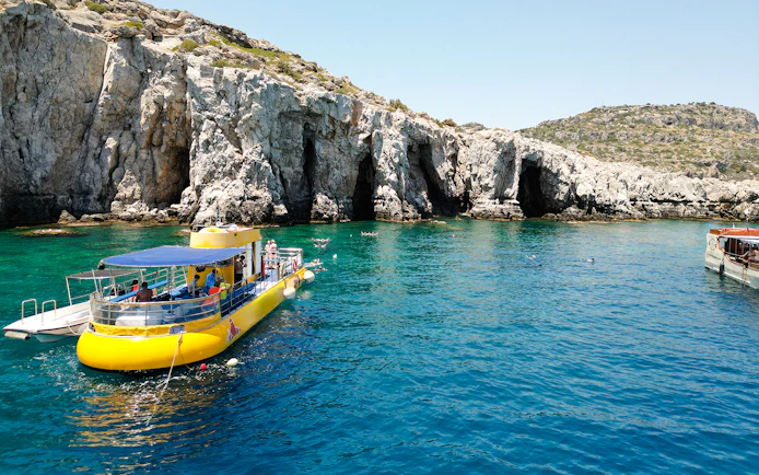 Yellow submarine cruise near rocky coast of Rhodes, Greece, with swimmers in clear blue water.