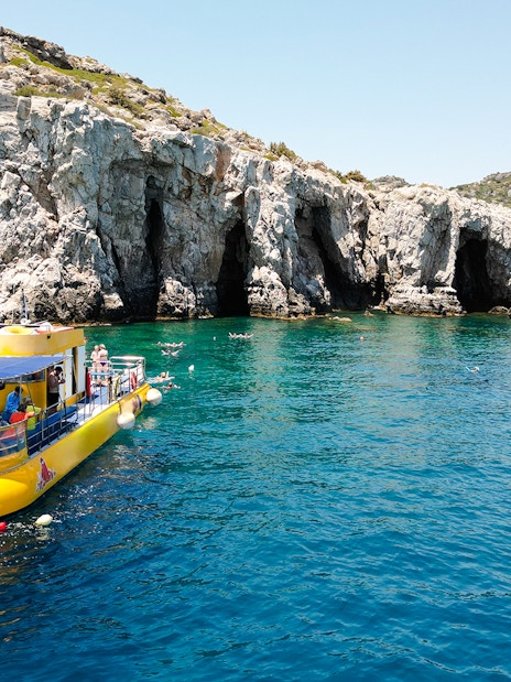 Yellow submarine cruise near rocky coast of Rhodes, Greece, with swimmers in clear blue water.