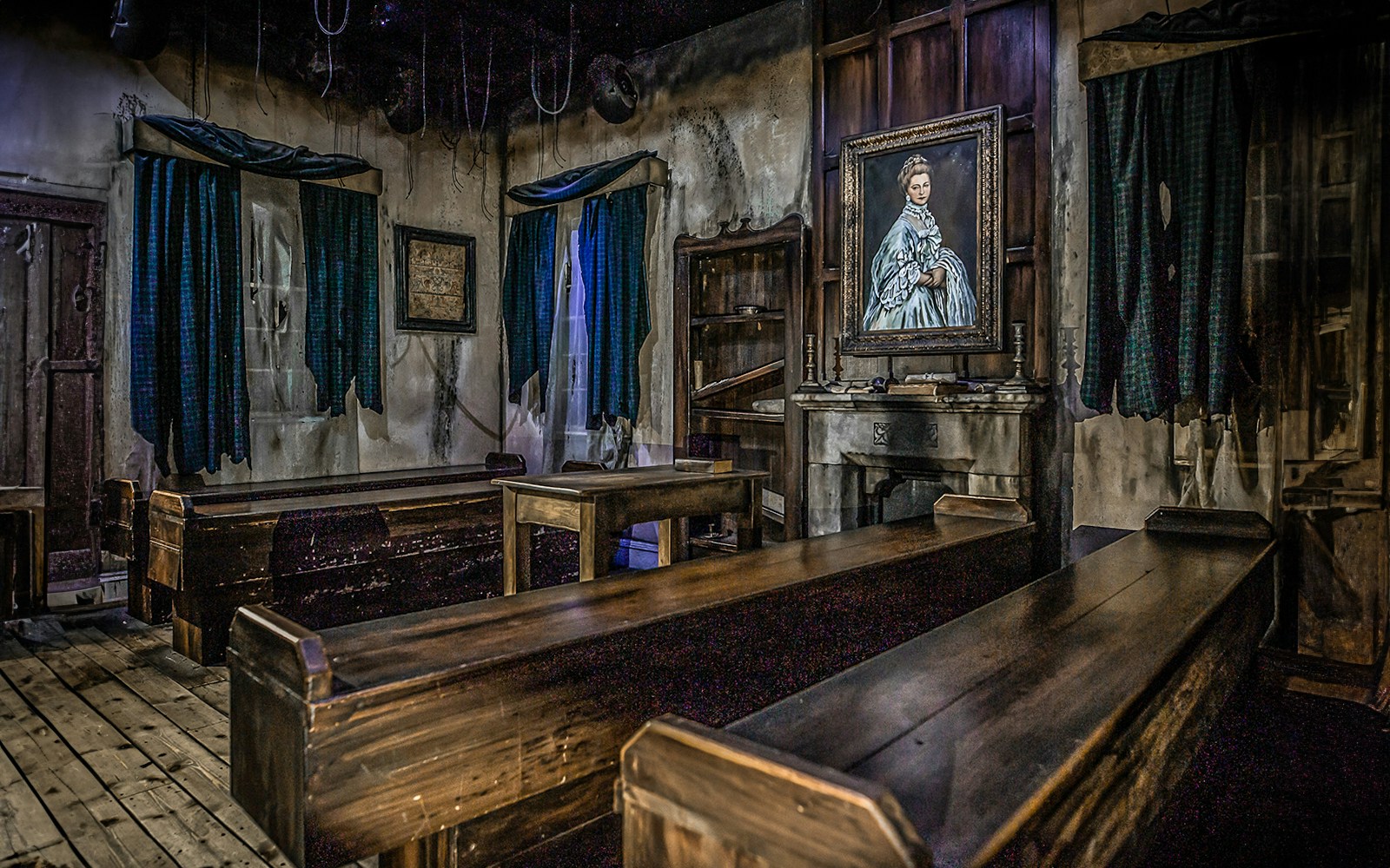Edinburgh Dungeon room with wooden benches and a portrait of a woman on the wall.