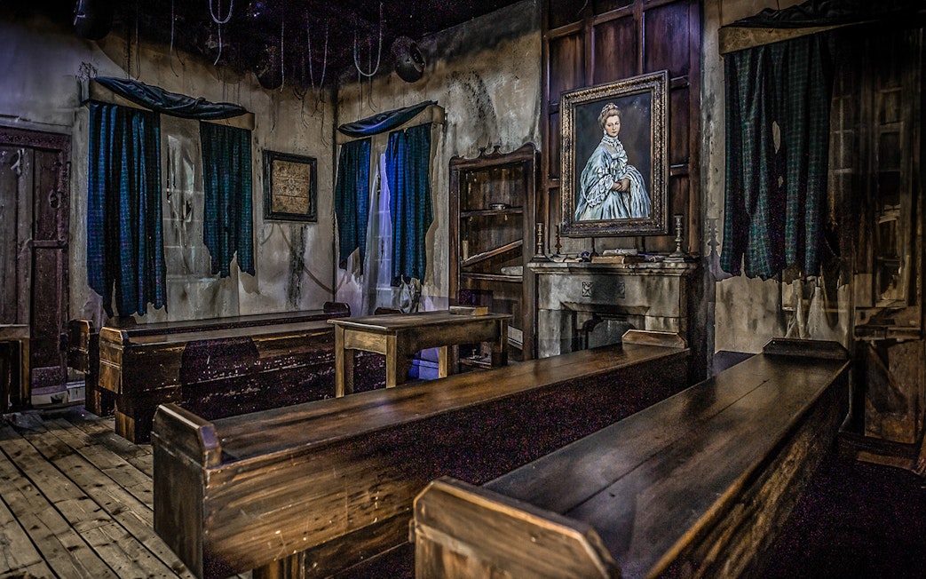 Edinburgh Dungeon room with wooden benches and a portrait of a woman on the wall.
