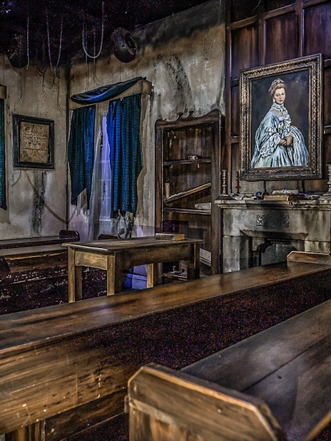 Edinburgh Dungeon room with wooden benches and a portrait of a woman on the wall.