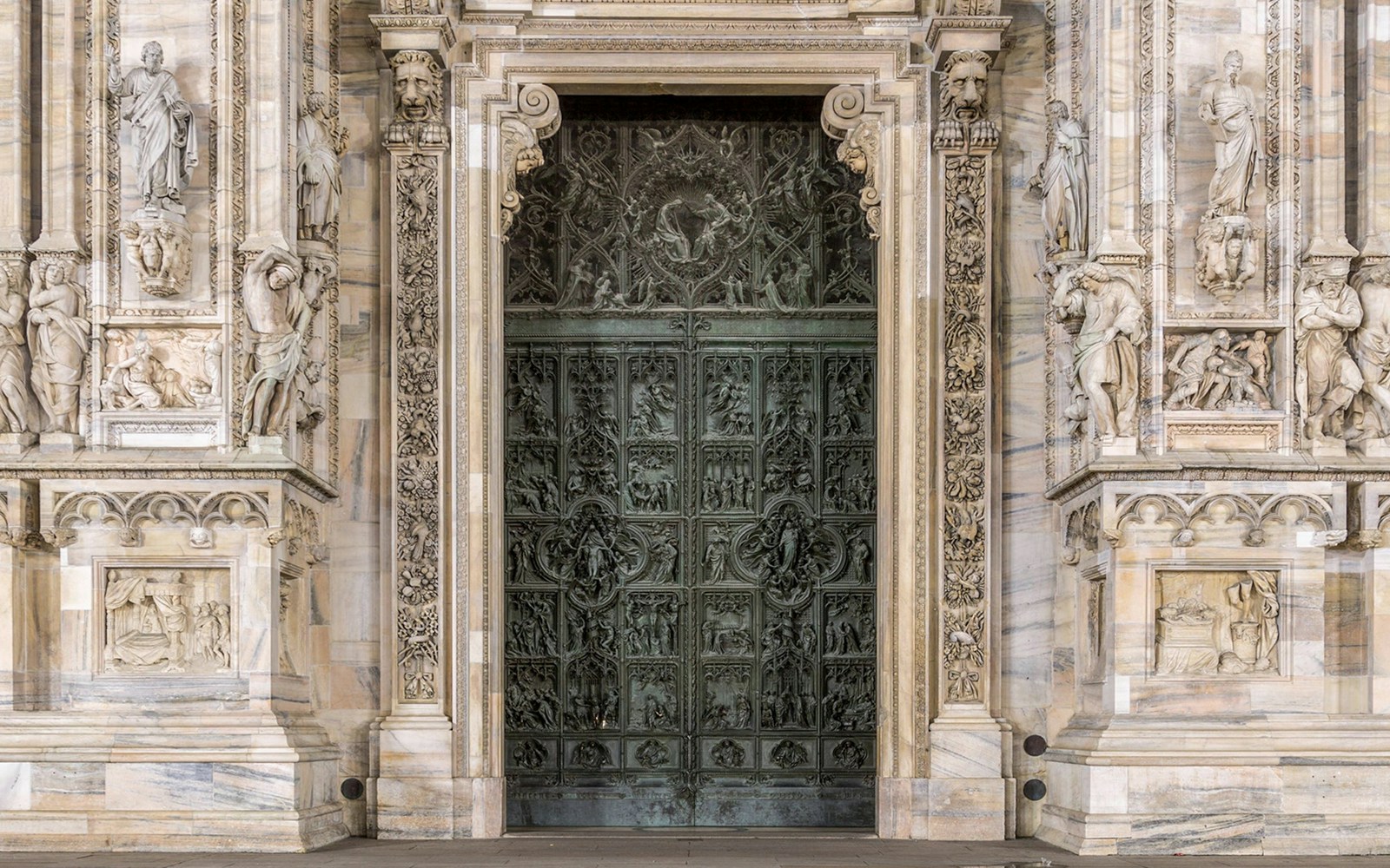 Main entrance of Duomo Milan Cathedral with intricate carvings and sculptures.