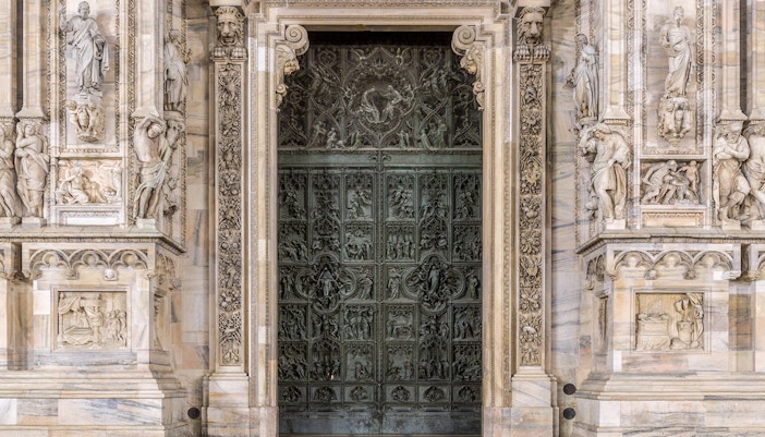 Main entrance of Duomo Milan Cathedral with intricate carvings and sculptures.