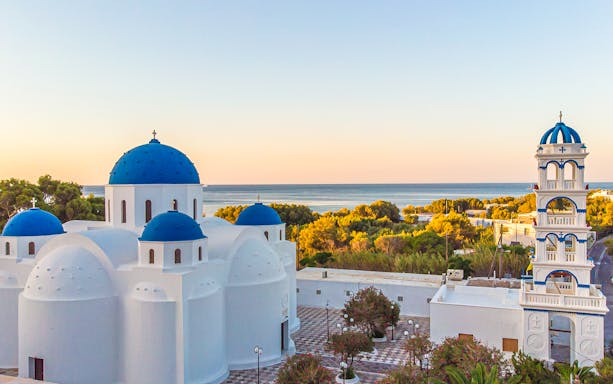 Blue-domed church and bell tower in Santorini with sea view at sunset.