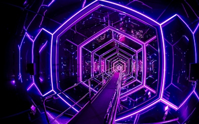 Neon-lit tunnel inside Amaze Amsterdam with geometric patterns.