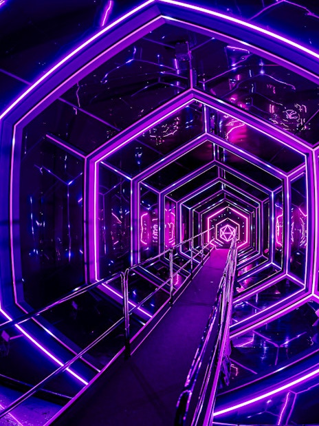 Neon-lit tunnel inside Amaze Amsterdam with geometric patterns.