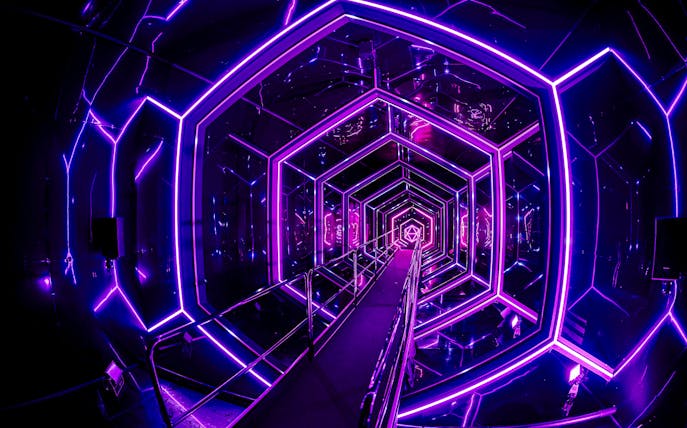 Neon-lit tunnel inside Amaze Amsterdam with geometric patterns.