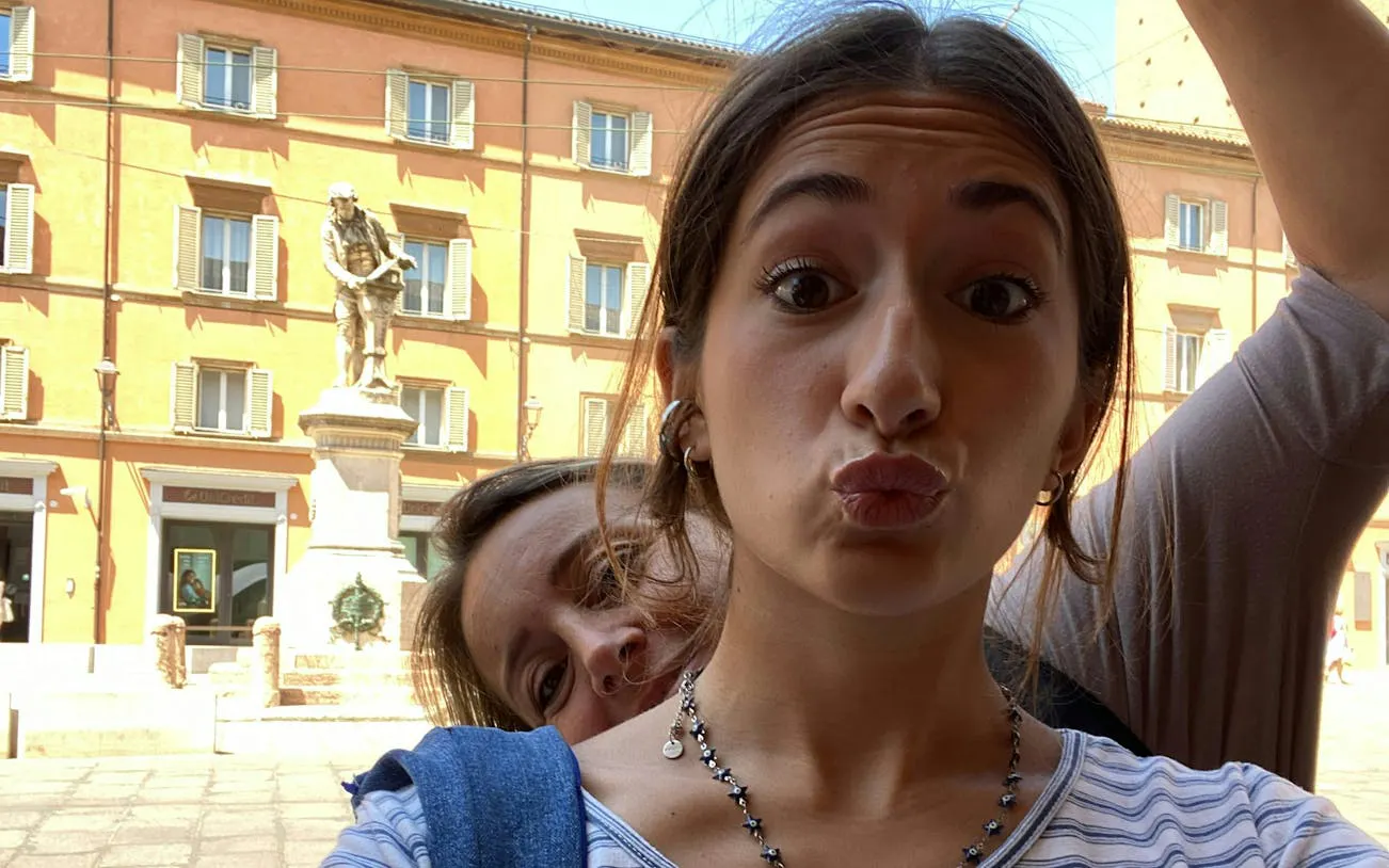 Two people taking a selfie in front of a statue in Bologna, Italy.