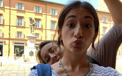 Two people taking a selfie in front of a statue in Bologna, Italy.