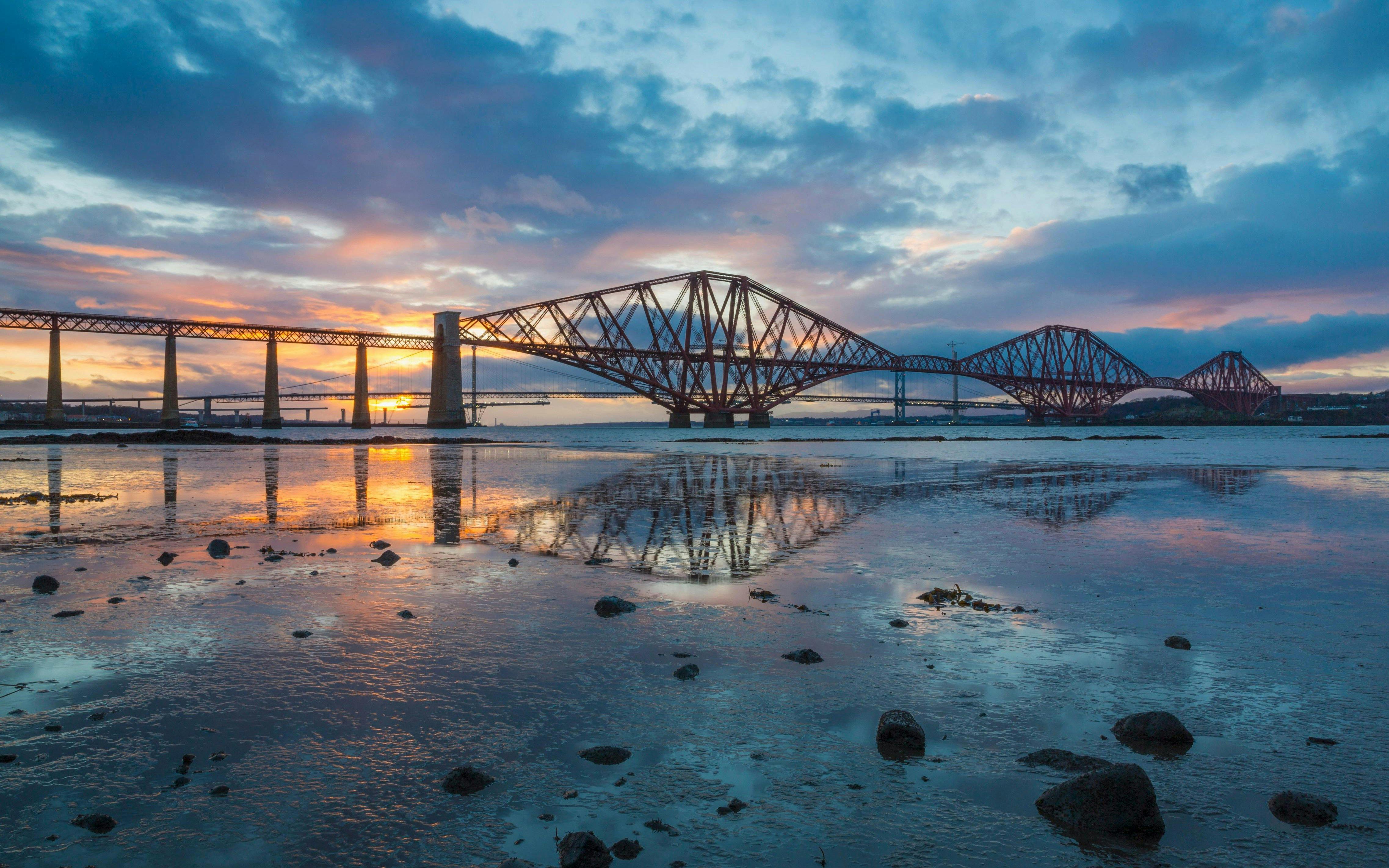Forth Bridge at sunset reflecting on the water in Scotland.