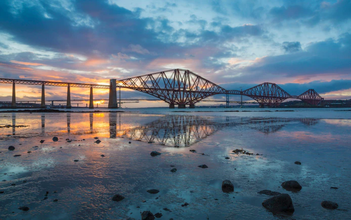 Forth Bridge at sunset reflecting on the water in Scotland.