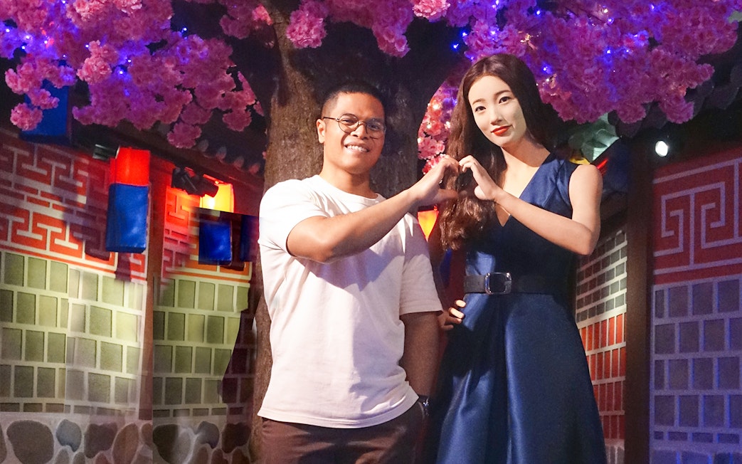 Man posing with wax figure at Madame Tussauds Singapore under cherry blossoms.