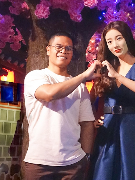 Man posing with wax figure at Madame Tussauds Singapore under cherry blossoms.
