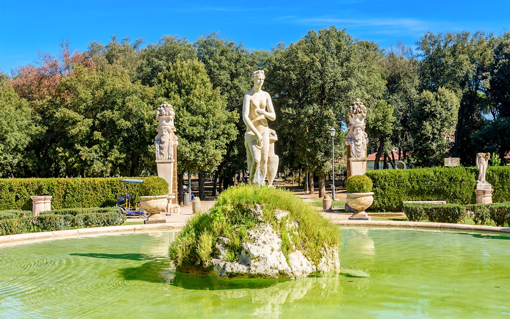 Statue and fountain in Borghese Gardens, Rome, surrounded by greenery.