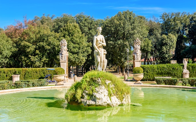 Statue and fountain in Borghese Gardens, Rome, surrounded by greenery.