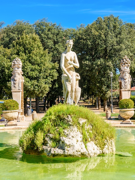 Statue and fountain in Borghese Gardens, Rome, surrounded by greenery.