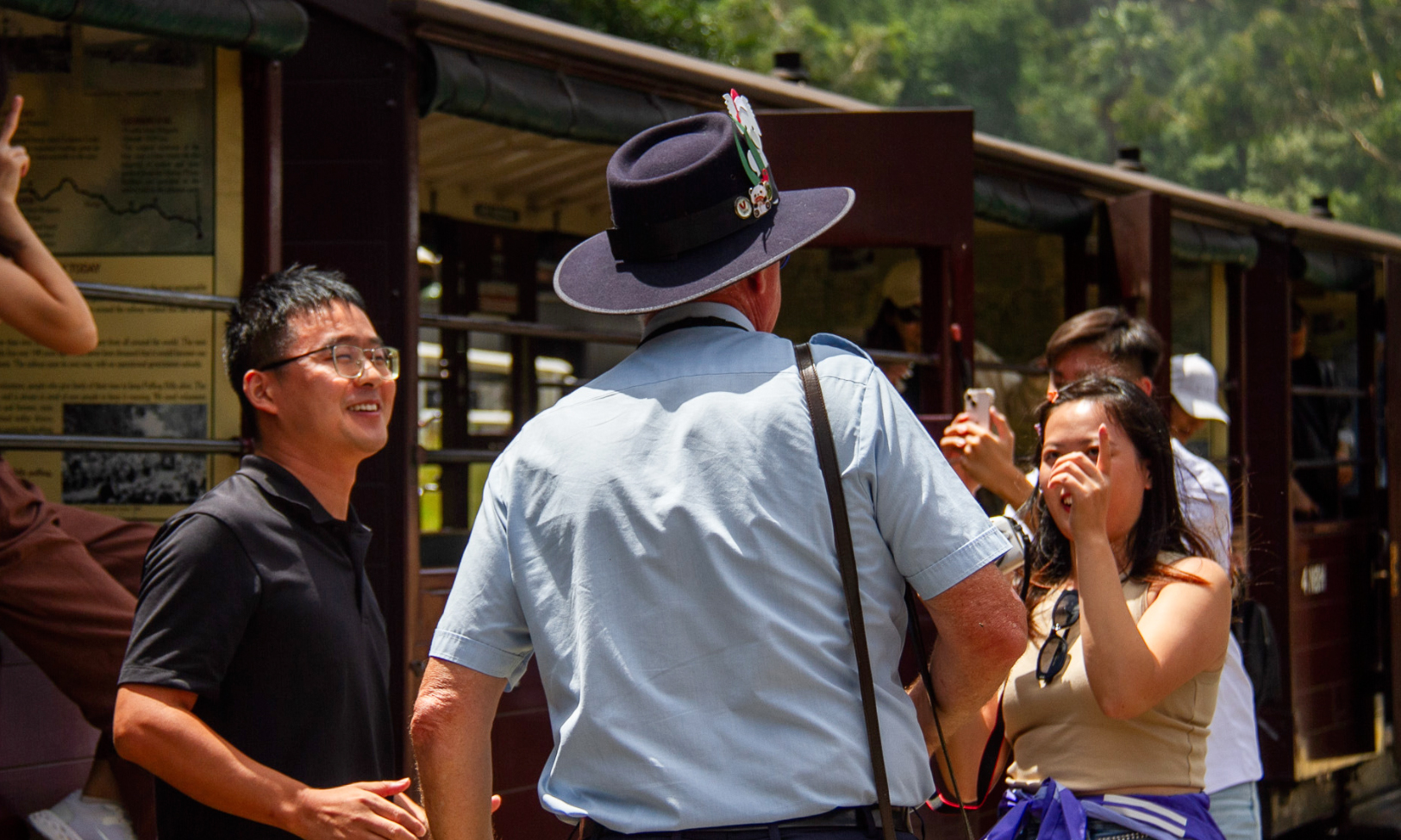 Puffing Billy tour guide in uniform converses with passengers on the station platform.