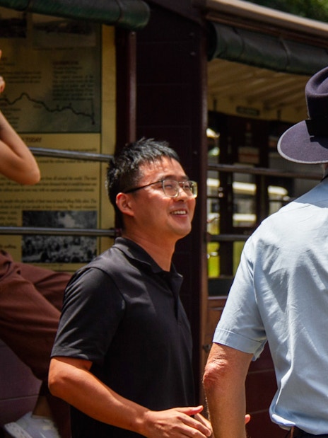 Puffing Billy tour guide in uniform converses with passengers on the station platform.