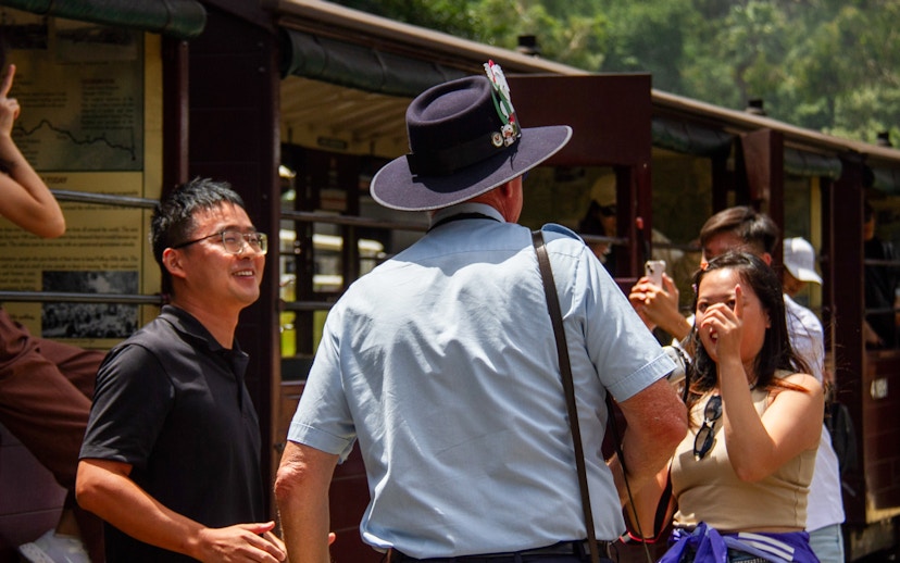 Puffing Billy tour guide in uniform converses with passengers on the station platform.