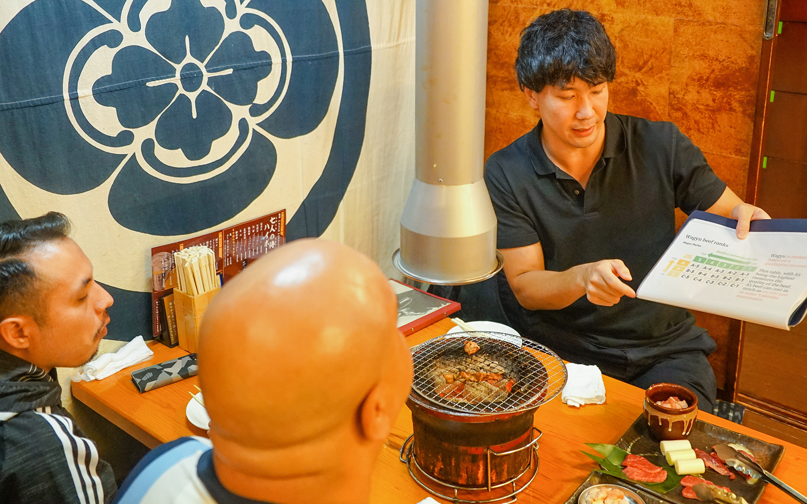 Guide explaining Wagyu beef classification to tourists at a Japanese restaurant.