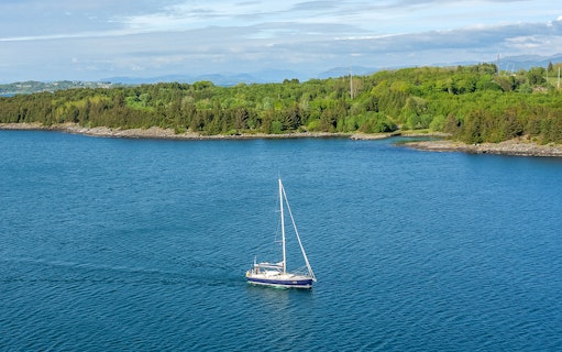 Sailboat on Stavanger Fjord with lush green shoreline in the background.