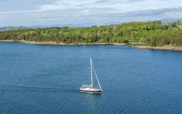Sailboat on Stavanger Fjord with lush green shoreline in the background.