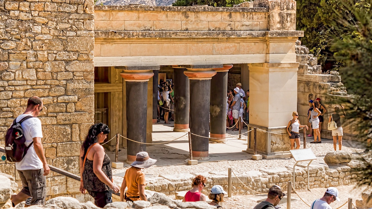 Visitors exploring ancient ruins at Knossos Palace Archaeological Site, Crete, during a guided tour.