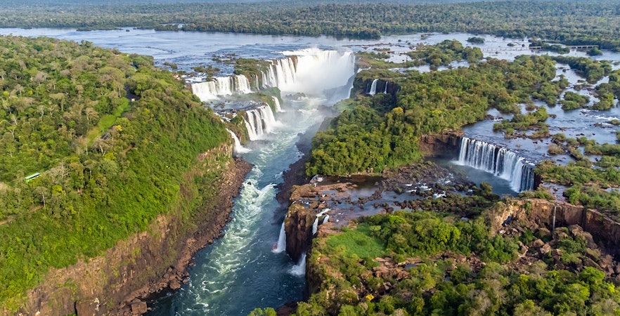 Iguazu Falls cascading between Brazil and Argentina, lush greenery surrounding.