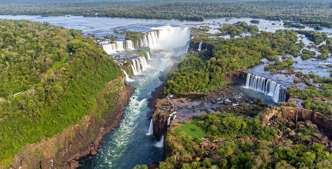 Iguazu Falls cascading between Brazil and Argentina, lush greenery surrounding.