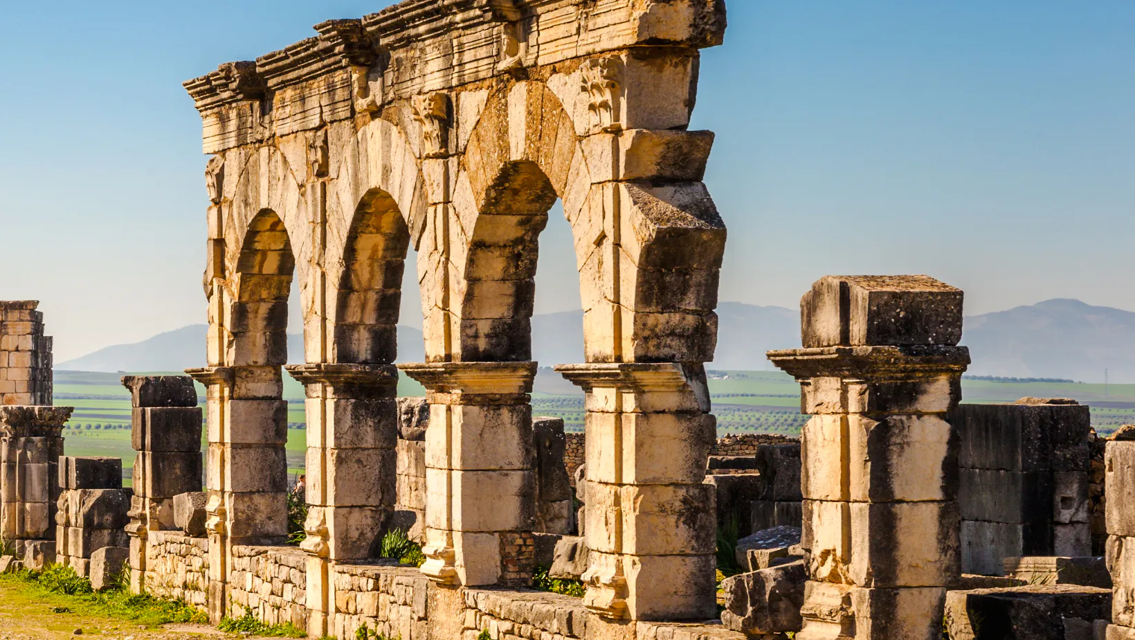 Ancient Roman arches at Volubilis near Fes, Morocco, with distant hills.